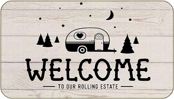 A black and beige doormat with a whimsical design that includes a vintage camper, trees, and the text 'WELCOME TO OUR ROLLING ESTATE'.
