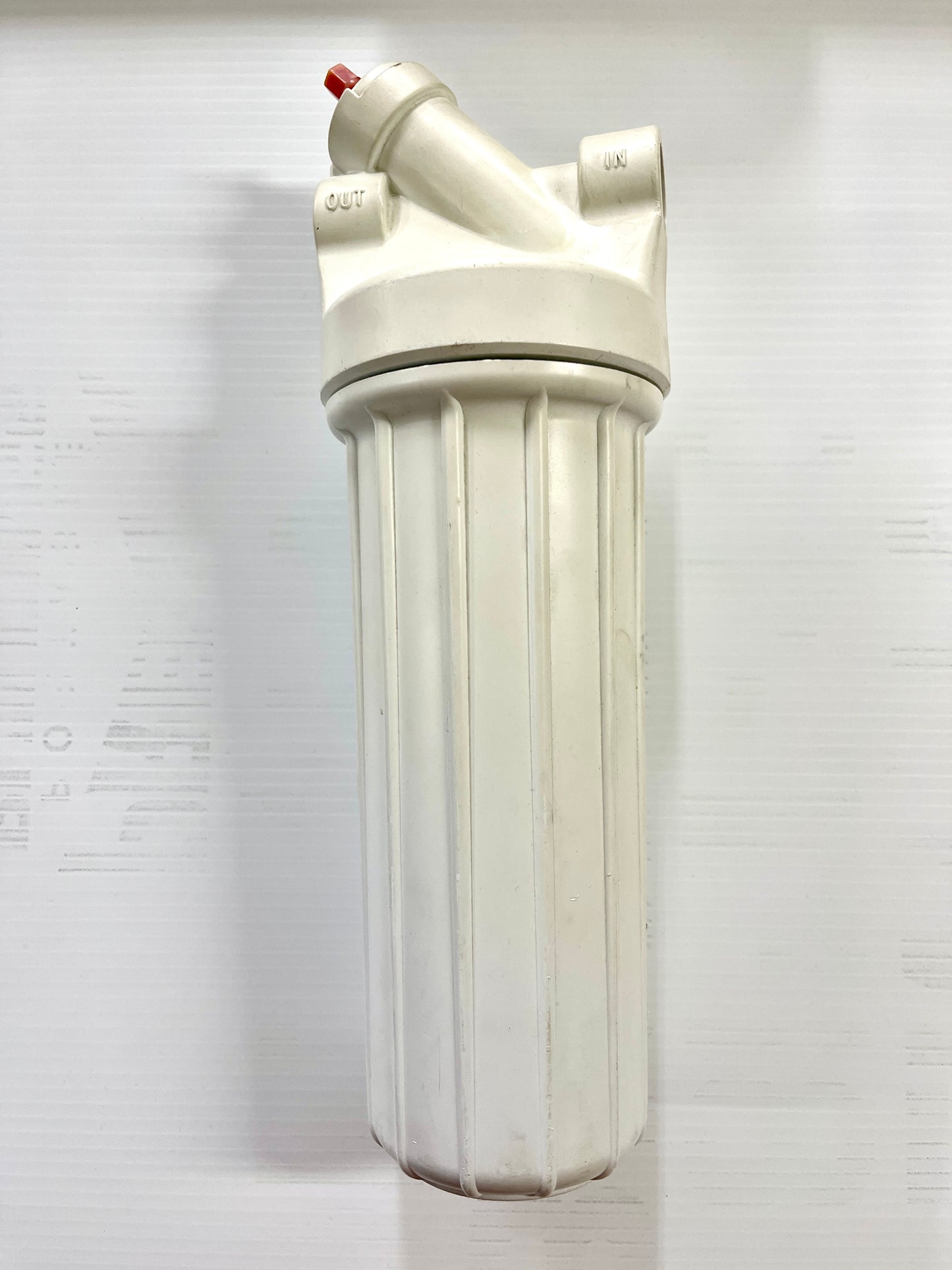 A white water filter canister with a twist off lid and two female threaded inlets for water lines.