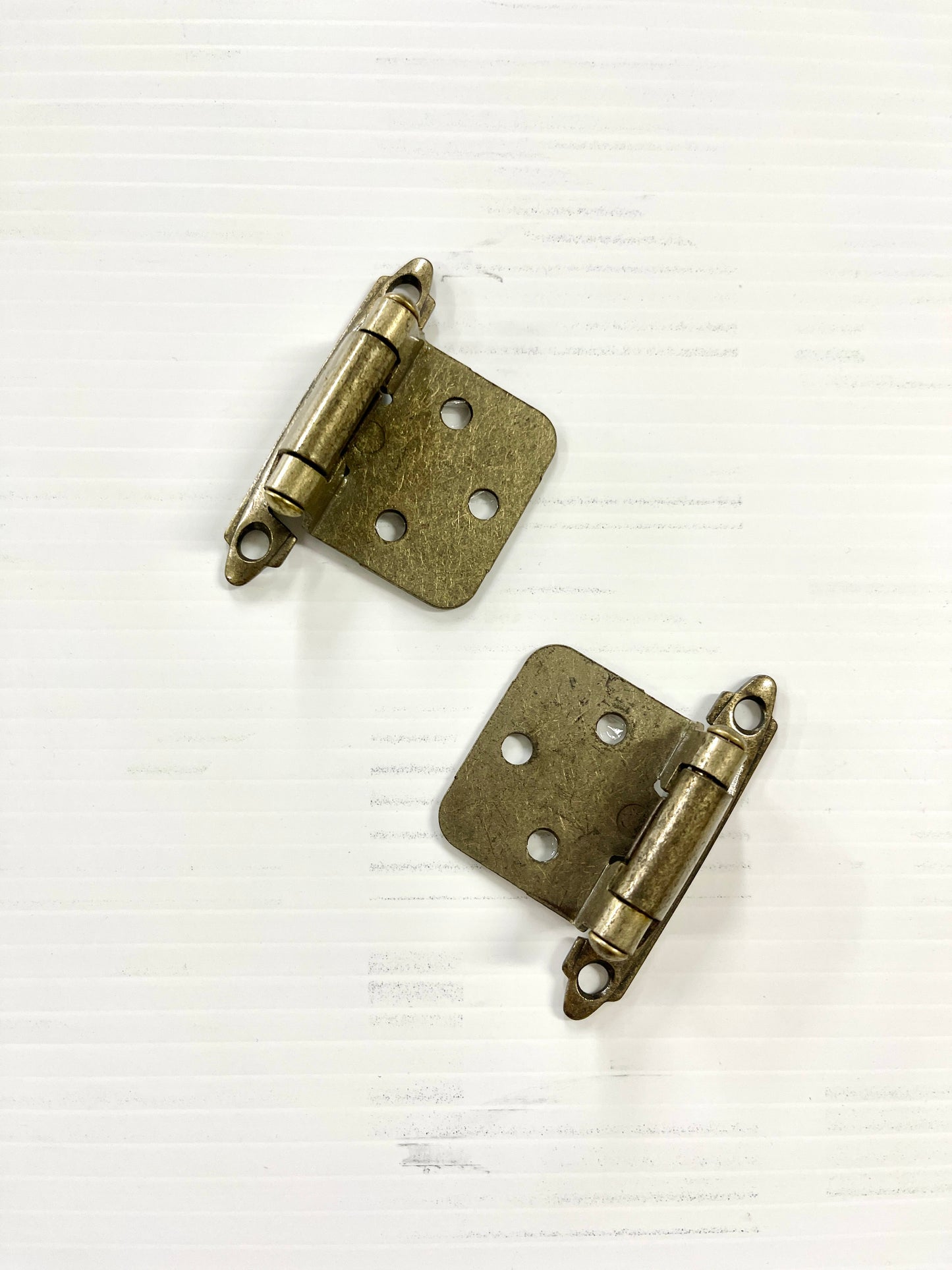 A pair of brass cabinet hinges with visible screw holes, set against a white background.