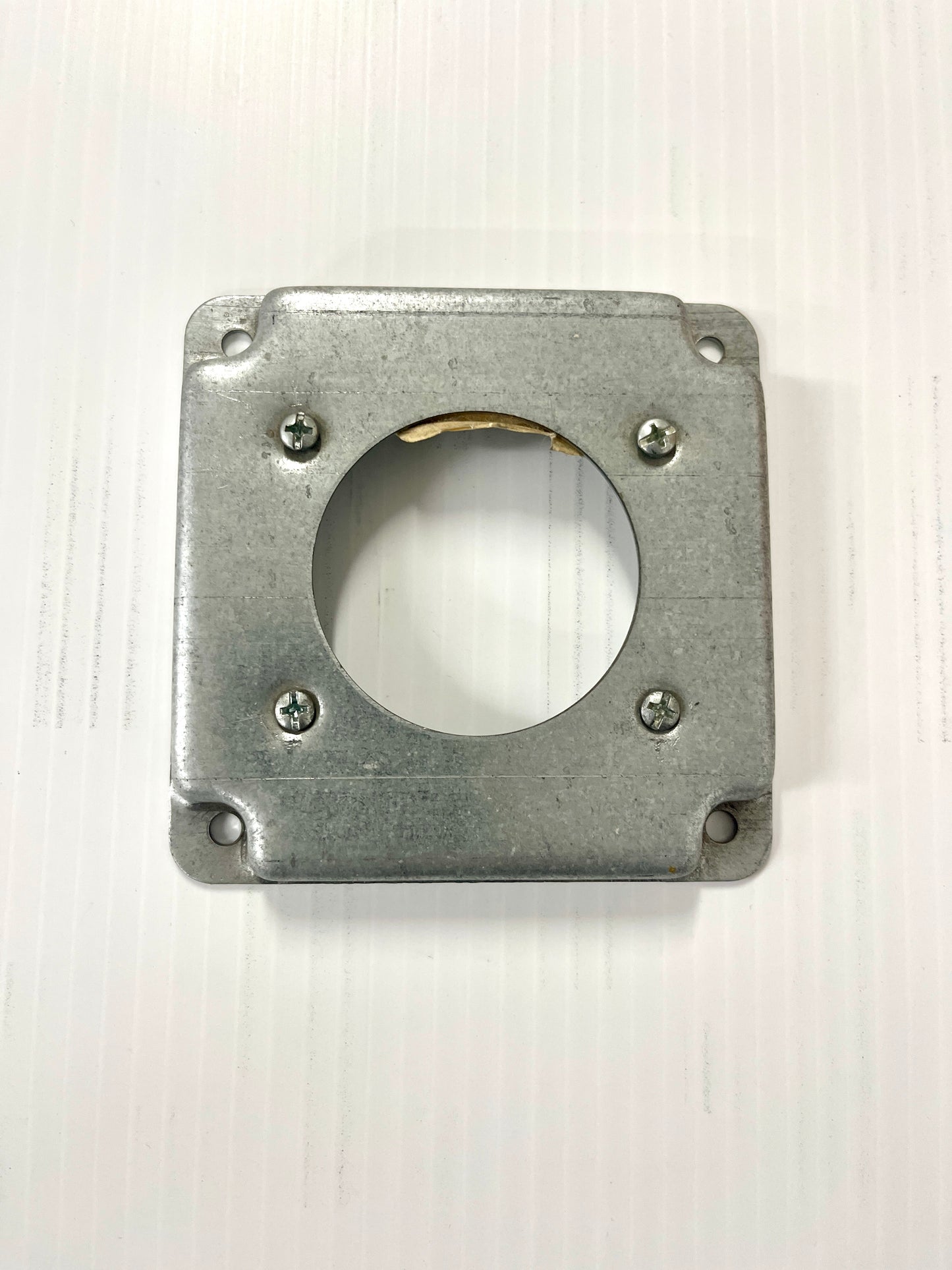 A square metal receptacle cover with a circle cutout in the center.