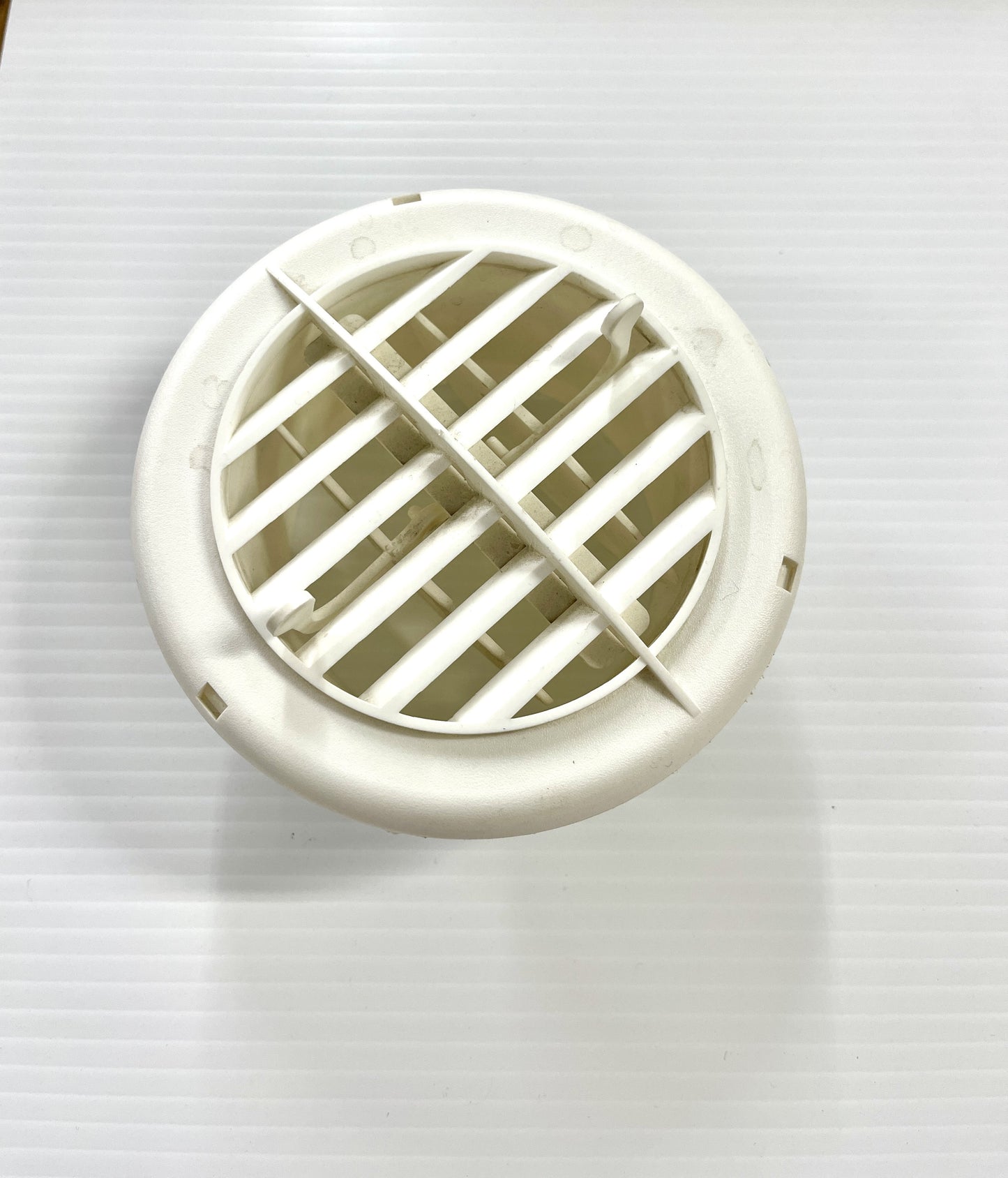 A white ceiling register/vent with a grid-like pattern and a central damper mechanism.