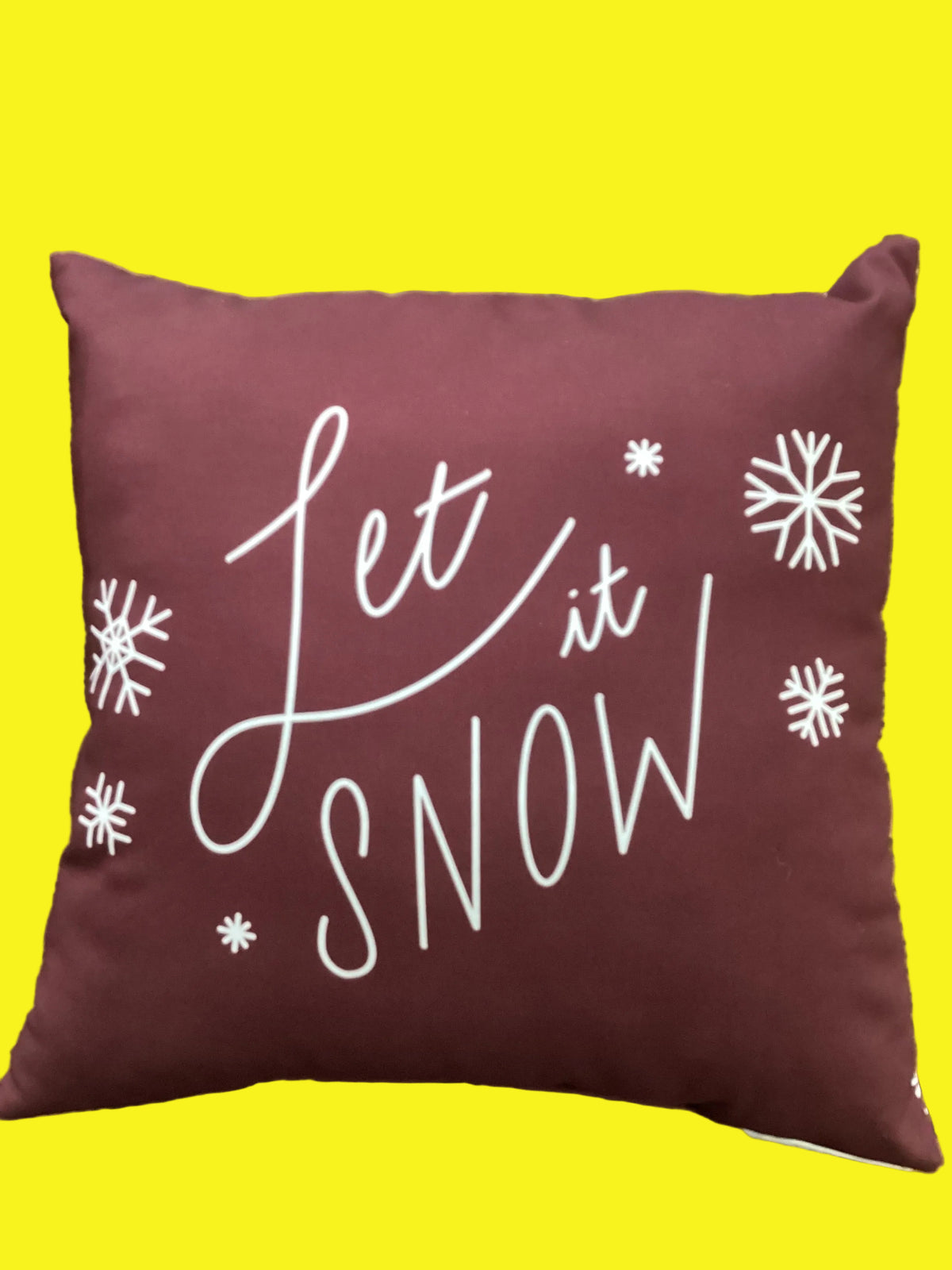 Maroon pillow with snow flakes and text reading "Let It Snow"