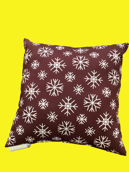 A square throw pillow with a white snowflake pattern on a dark burgundy background.